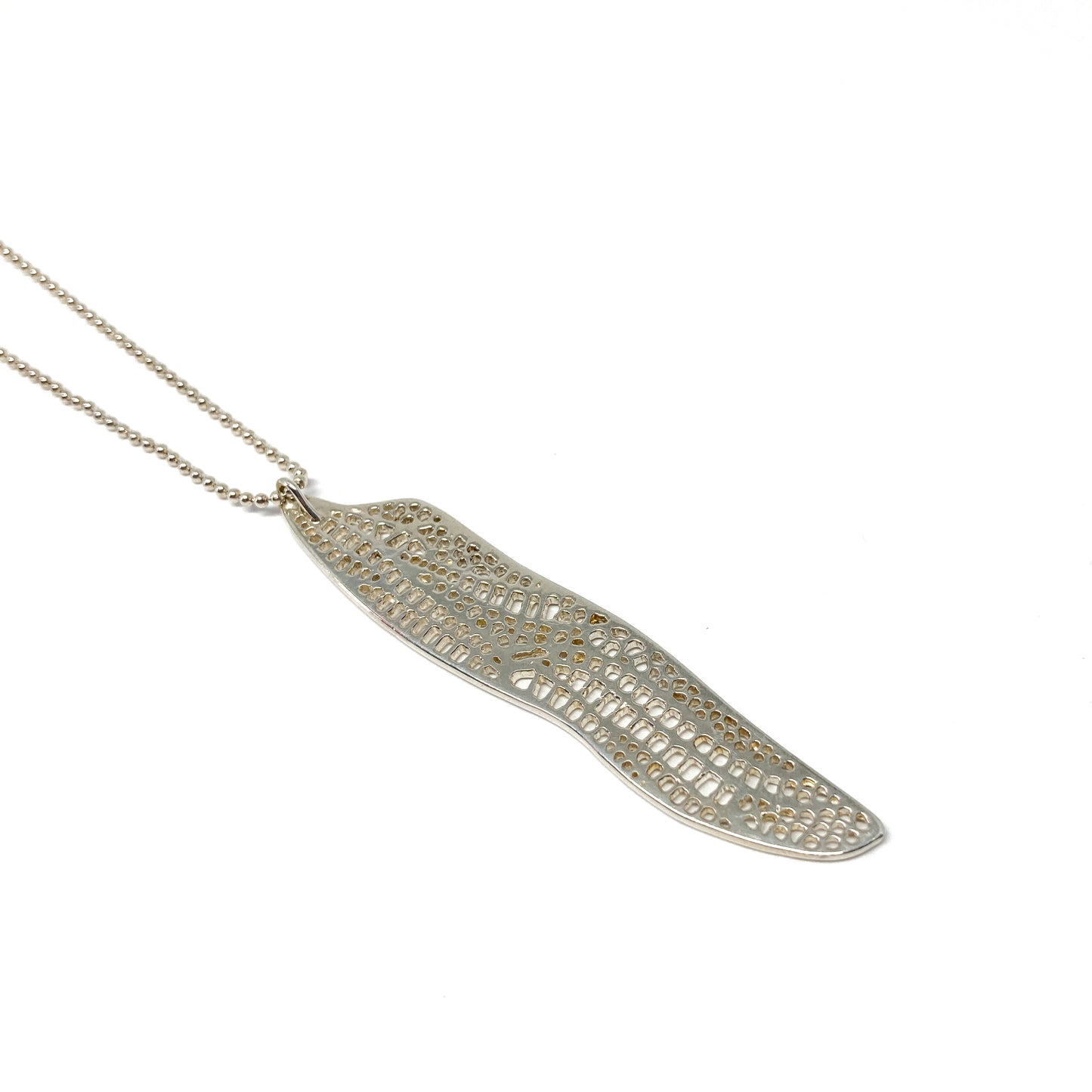 A silver ball chain necklace features a long, curved pendant with an intricate, openwork dragonfly wing design.