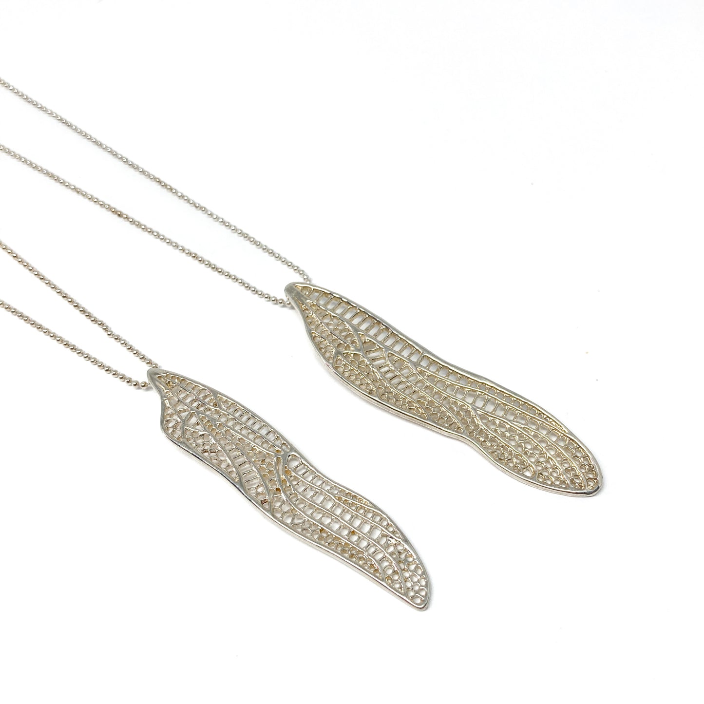 Two delicate silver necklaces feature horizontal pendants shaped like detailed dragonfly wings.