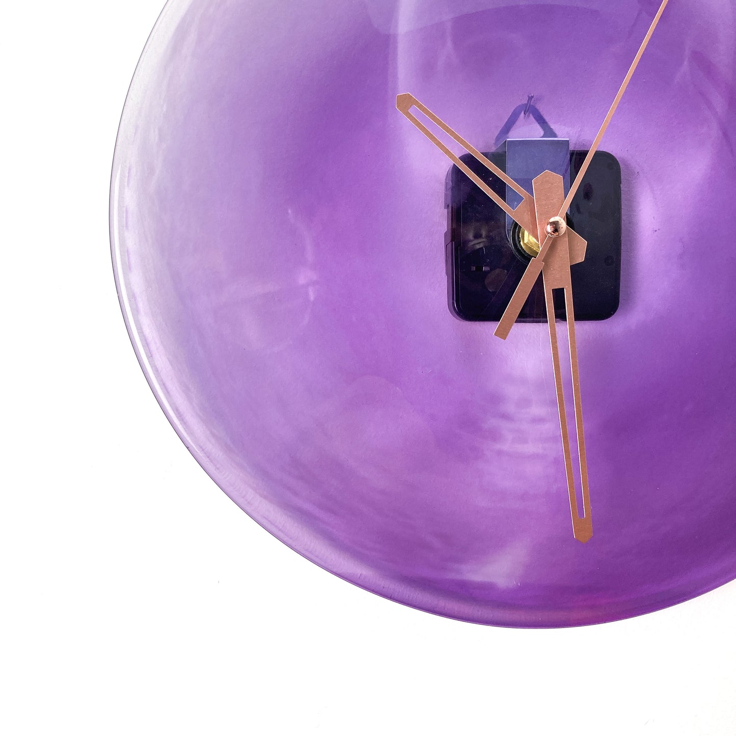 Close-up of a round purple glass clock face with a lighter center, showing thin gold-toned hour, minute, and second hands.