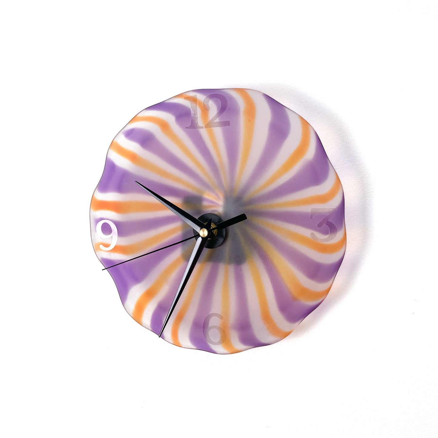 A round glass wall clock with radiating stripes of orange, purple, and white, featuring black hands and silver numerals.