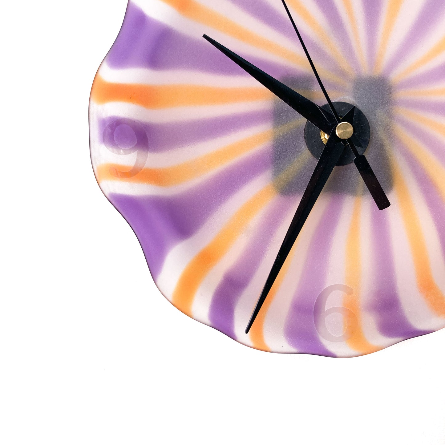 Close-up of a round glass clock face with radiating orange, purple, and white stripes, black hands, and visible silver numerals.