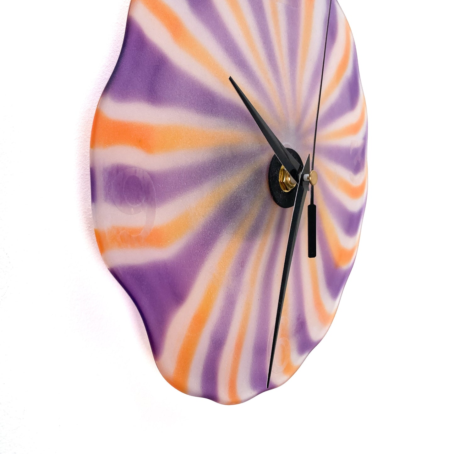 Side view of a round Hope Forstenzer glass clock with radiating orange, purple, and white stripes and black hands.