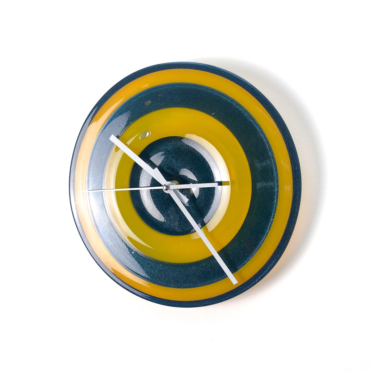 A round glass wall clock with concentric rings of yellow and blue, featuring white hands and no numerals.