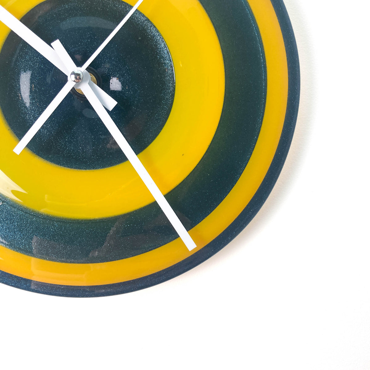 Close-up of a round glass clock face with concentric rings of blue and yellow, showing white hour, minute, and second hands.