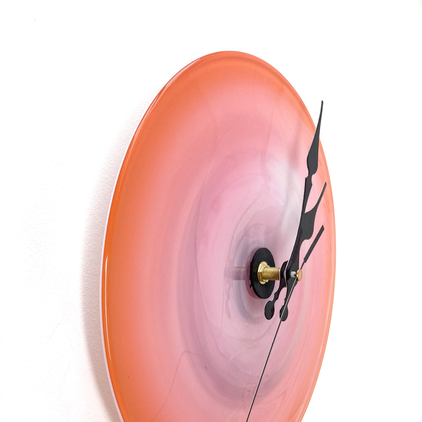 Side view of a round, large pink glass clock by Hope Forstenzer with a lighter center and ornate black hands.