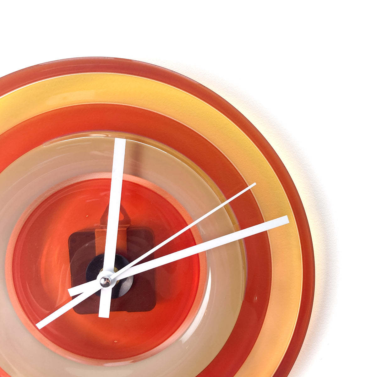 Close-up of a round glass clock face with concentric rings of red, orange, and beige, showing white hour, minute, and second hands.