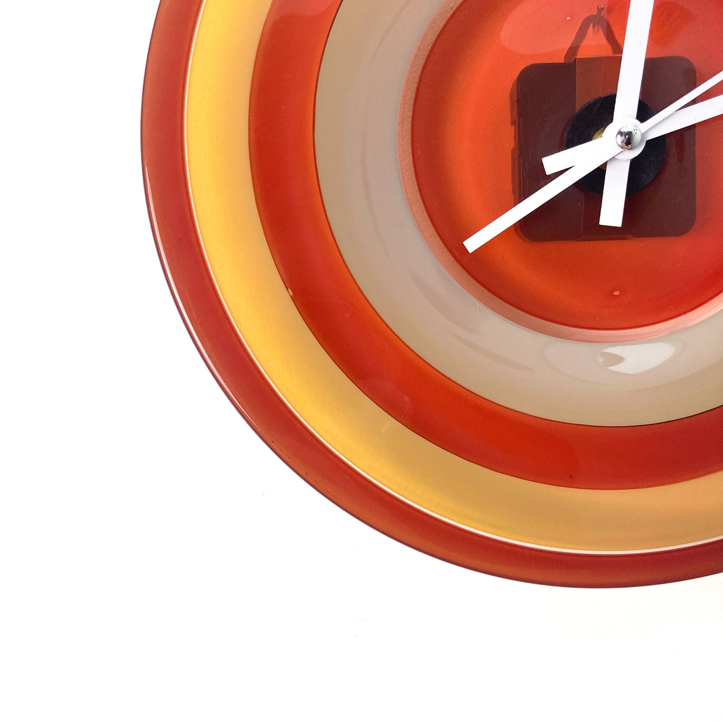 Close-up of a round glass clock face with concentric rings of red, yellow, and beige, showing white hour, minute, and second hands.