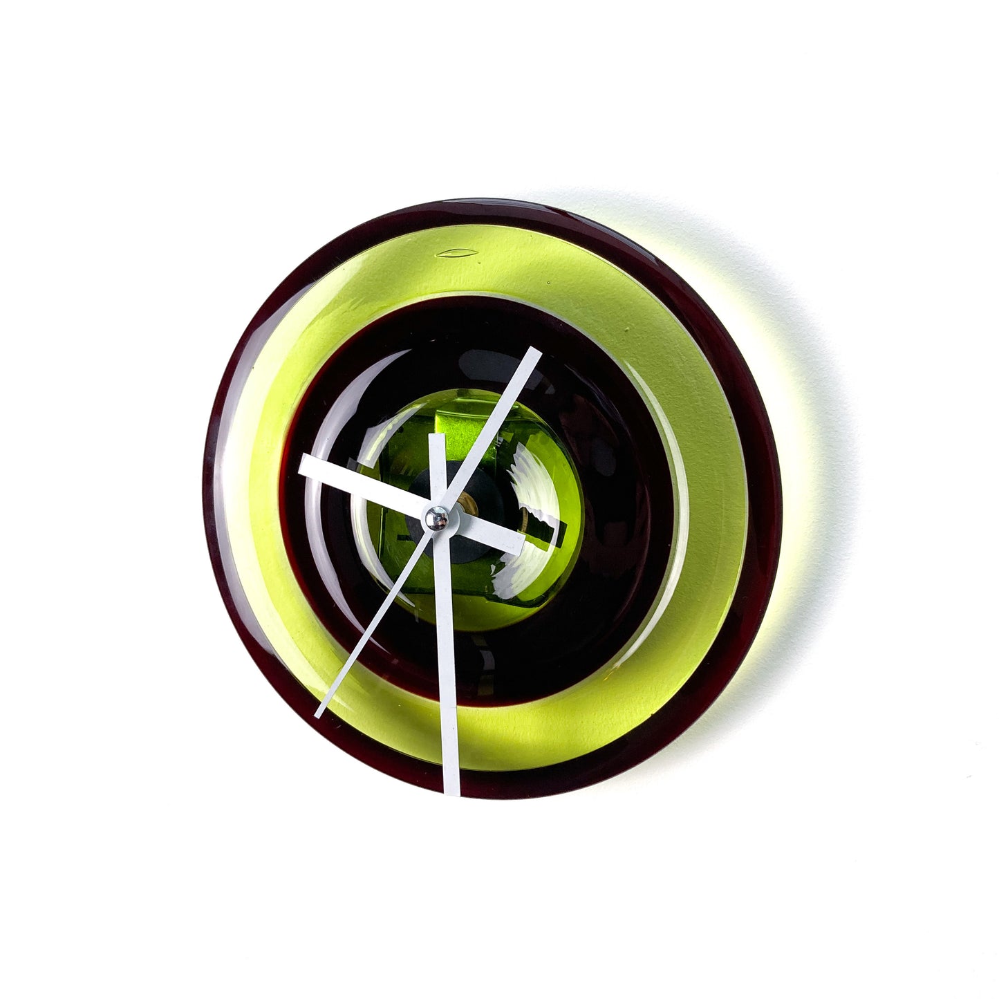 A round glass wall clock with concentric rings of lime green, dark red, and black, featuring white hands and no numerals.