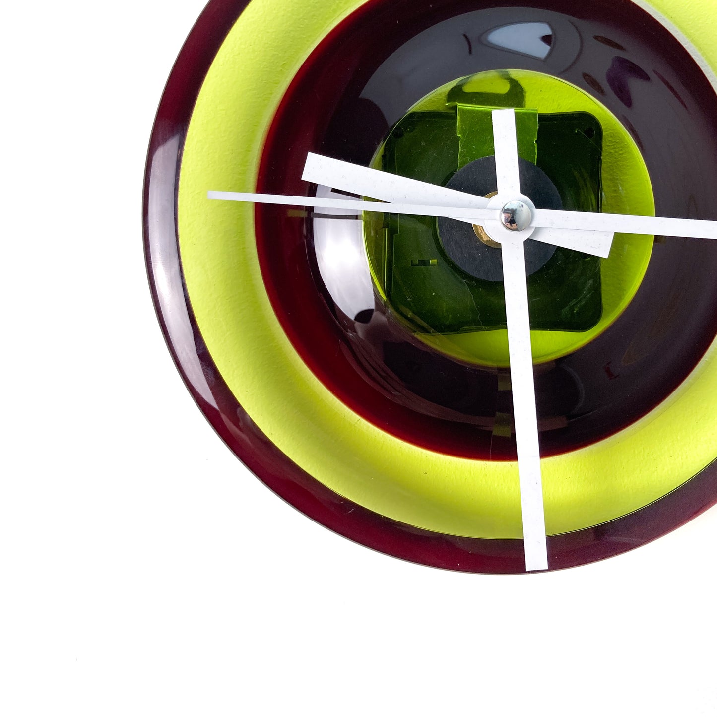 Close-up of a round glass clock face with concentric rings of lime green, dark red, and black, showing white hour, minute, and second hands.