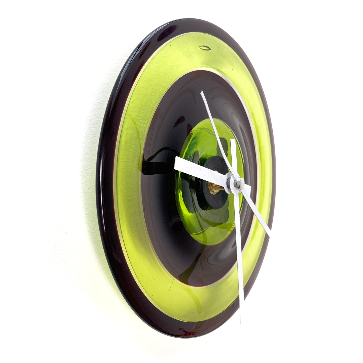 Side view of a round glass clock with concentric rings of lime green, dark red, and black, featuring white hands.