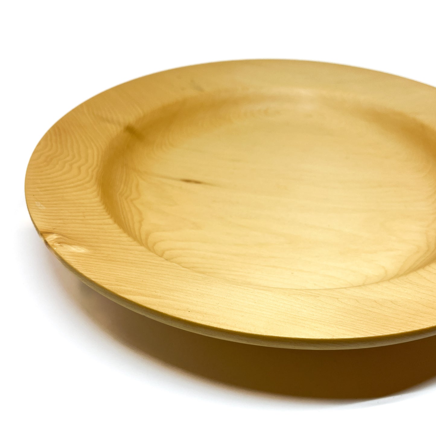An angled close-up view of a rimmed yellow cedar plate, showcasing its subtle grain.