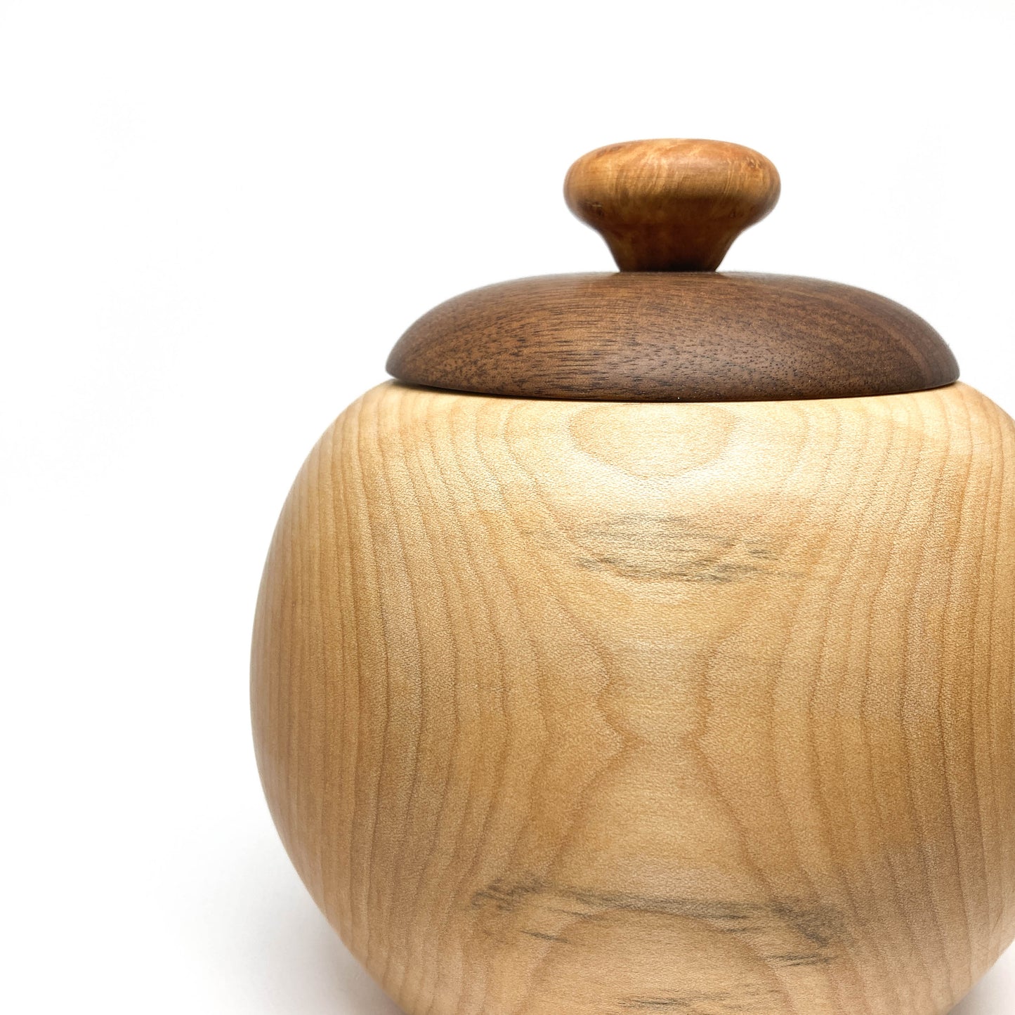 Close-up of a lidded maple bowl, showing the wood grain, with a dark walnut lid and knob.