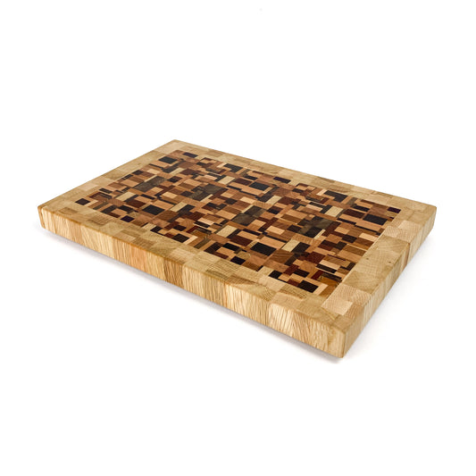 An end grain cutting board with a mosaic-like pattern of various wood tones, viewed from an angle.