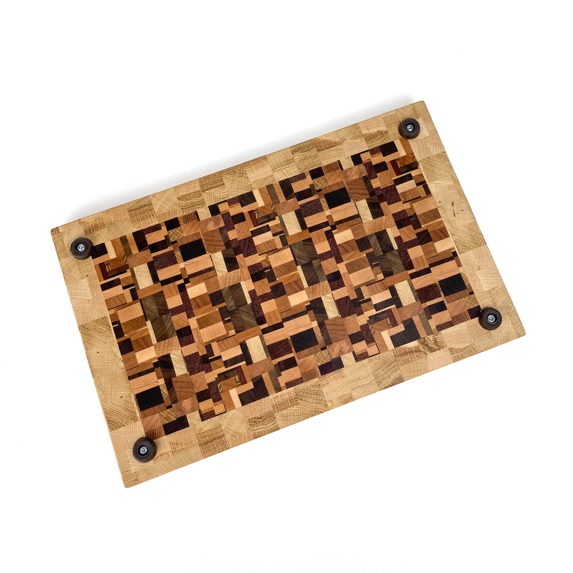 An overhead view of an end grain cutting board with a chaotic wood pattern and rubber feet.