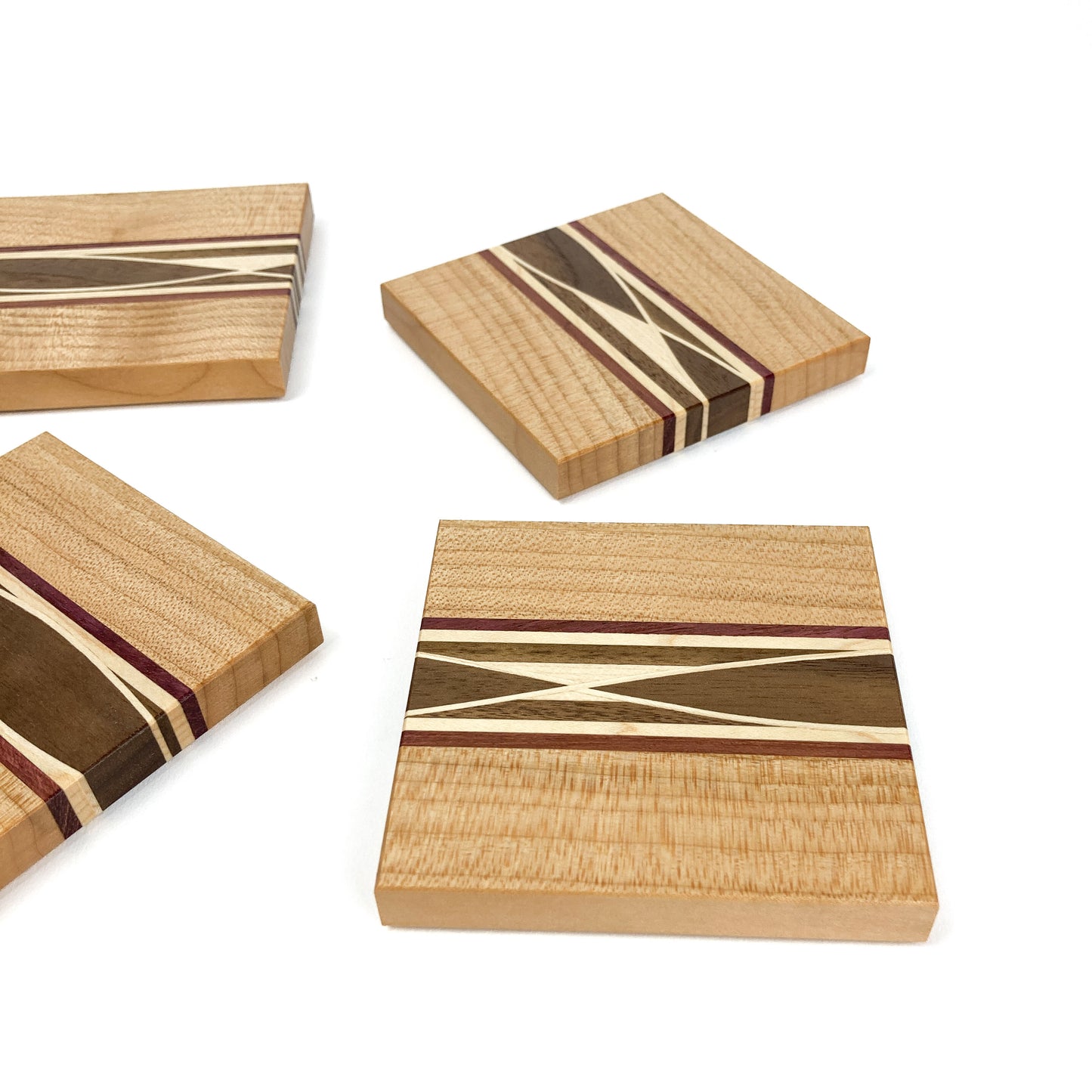Four individual light wood coasters featuring diverse inlaid patterns of different wood types.
