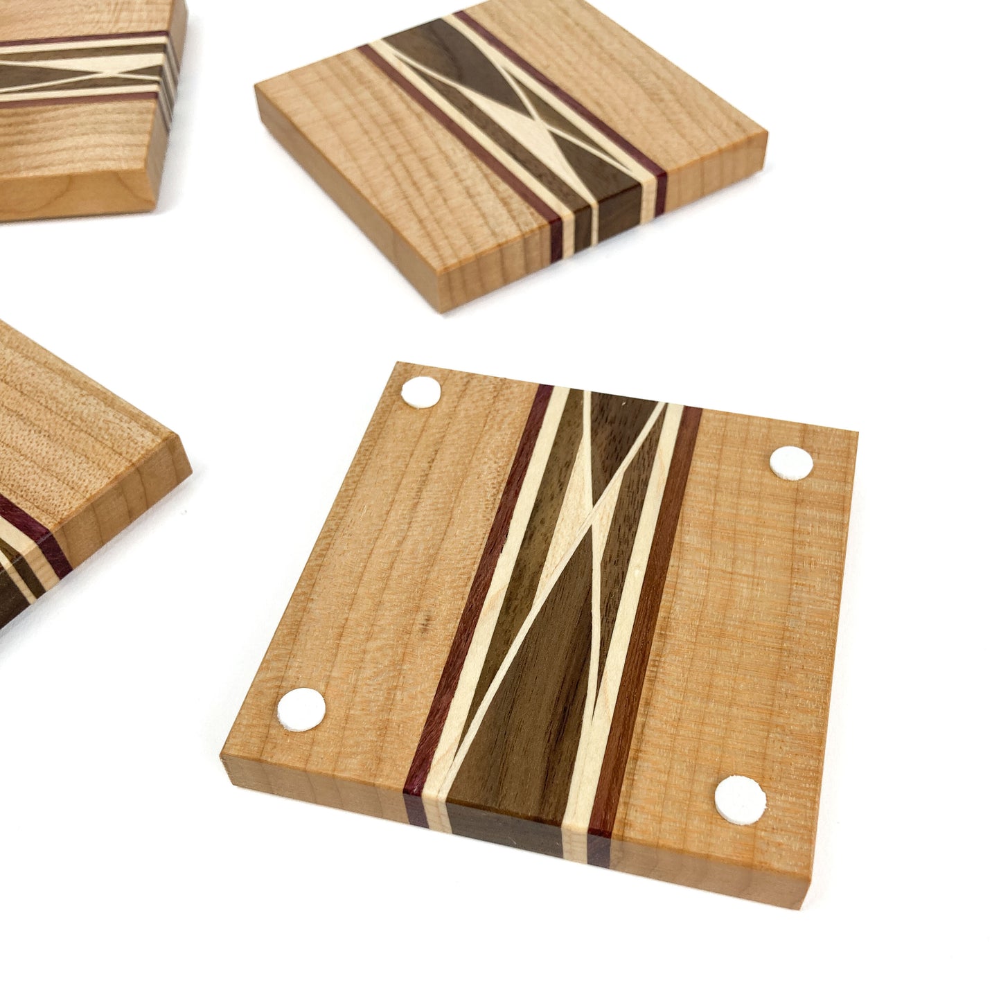 Top-down view of four light wood coasters with inlaid patterns and white protective feet on one.
