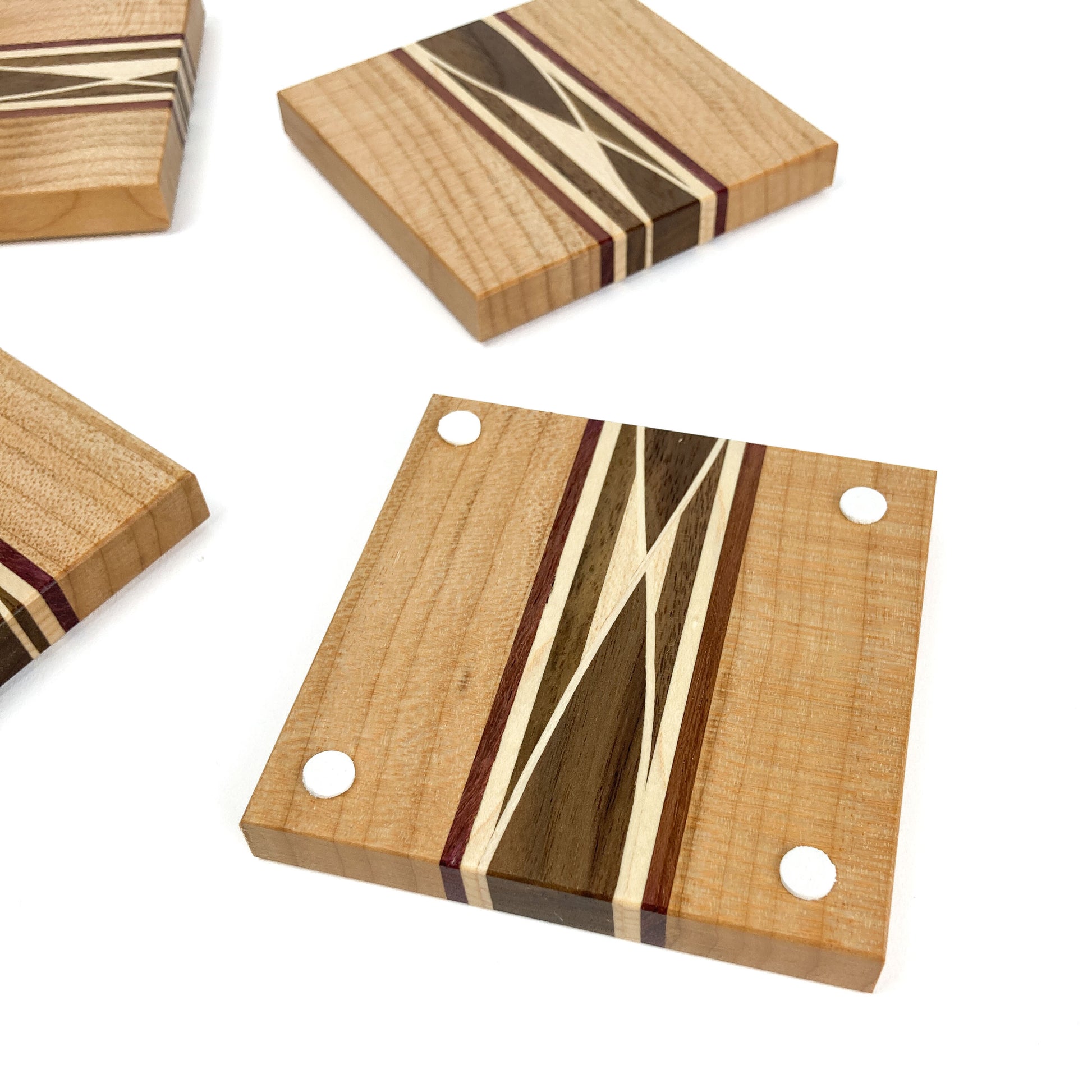 Top-down view of four light wood coasters with inlaid patterns and white protective feet on one.