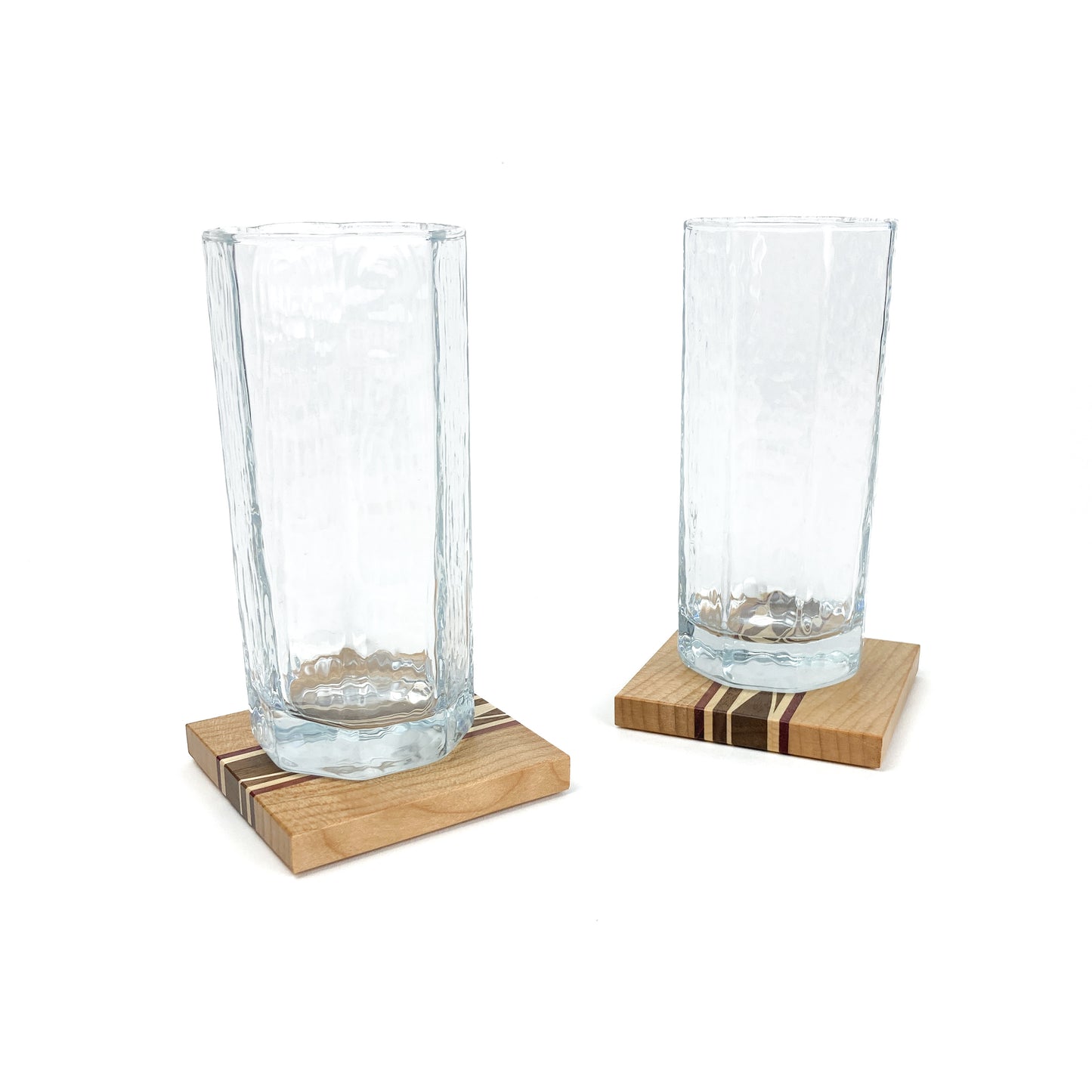 Two textured glass cups resting on individual light wood coasters with striped inlays.