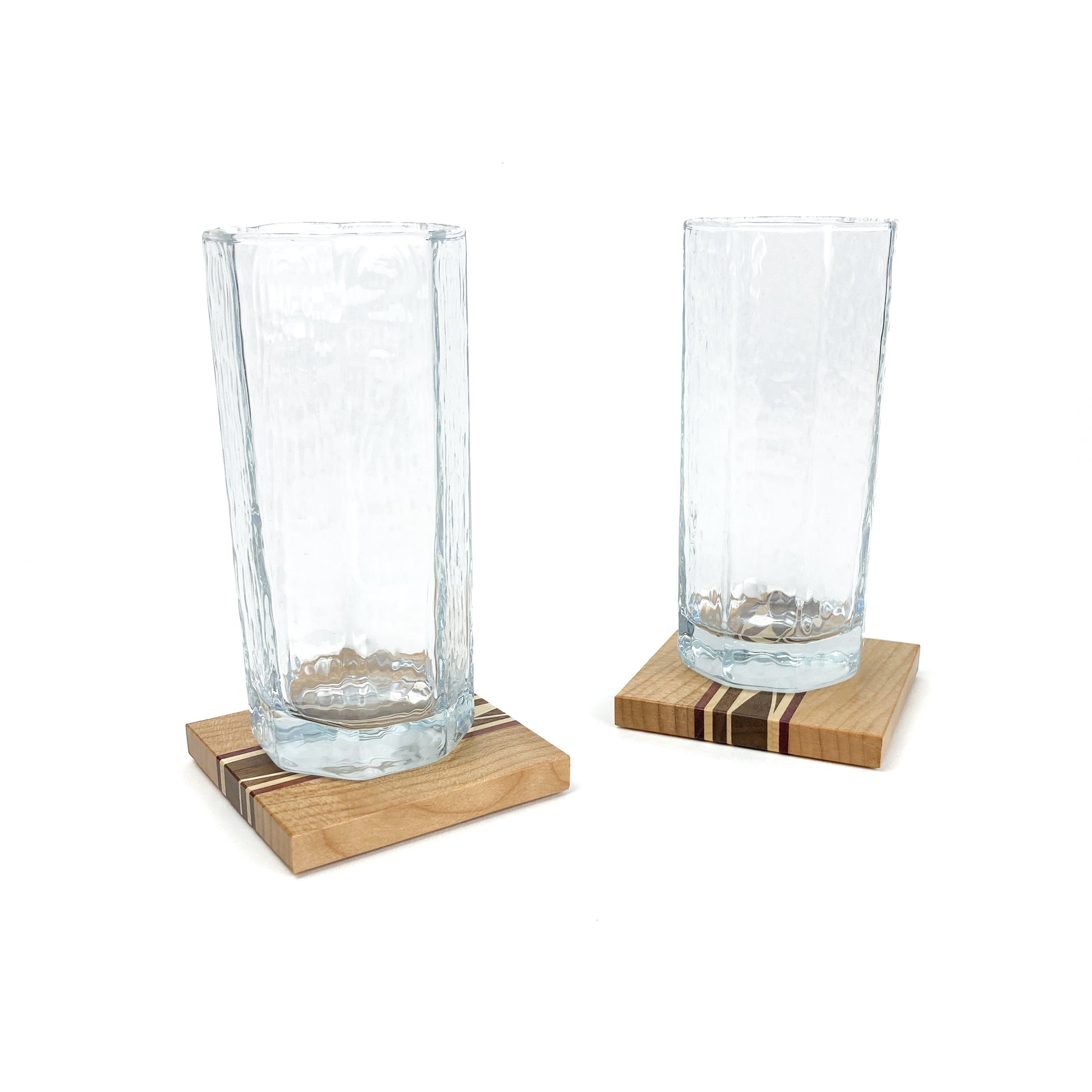 Two textured glass cups resting on individual light wood coasters with striped inlays.