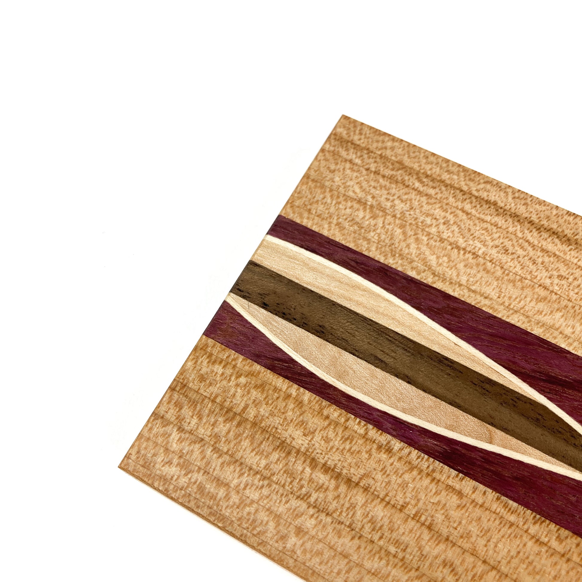 Close-up of a light wood coaster with a central inlay design featuring various wood tones and purple.