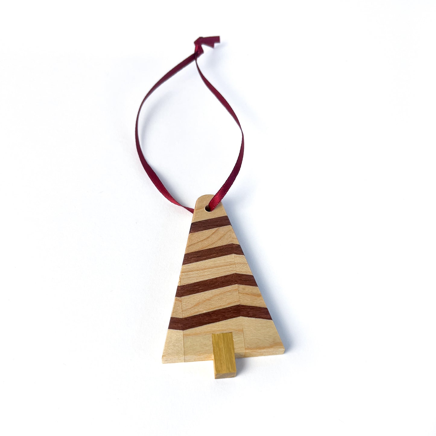 A wooden Christmas tree ornament made of light and dark wood stripes, with a light-colored trunk and a red ribbon.