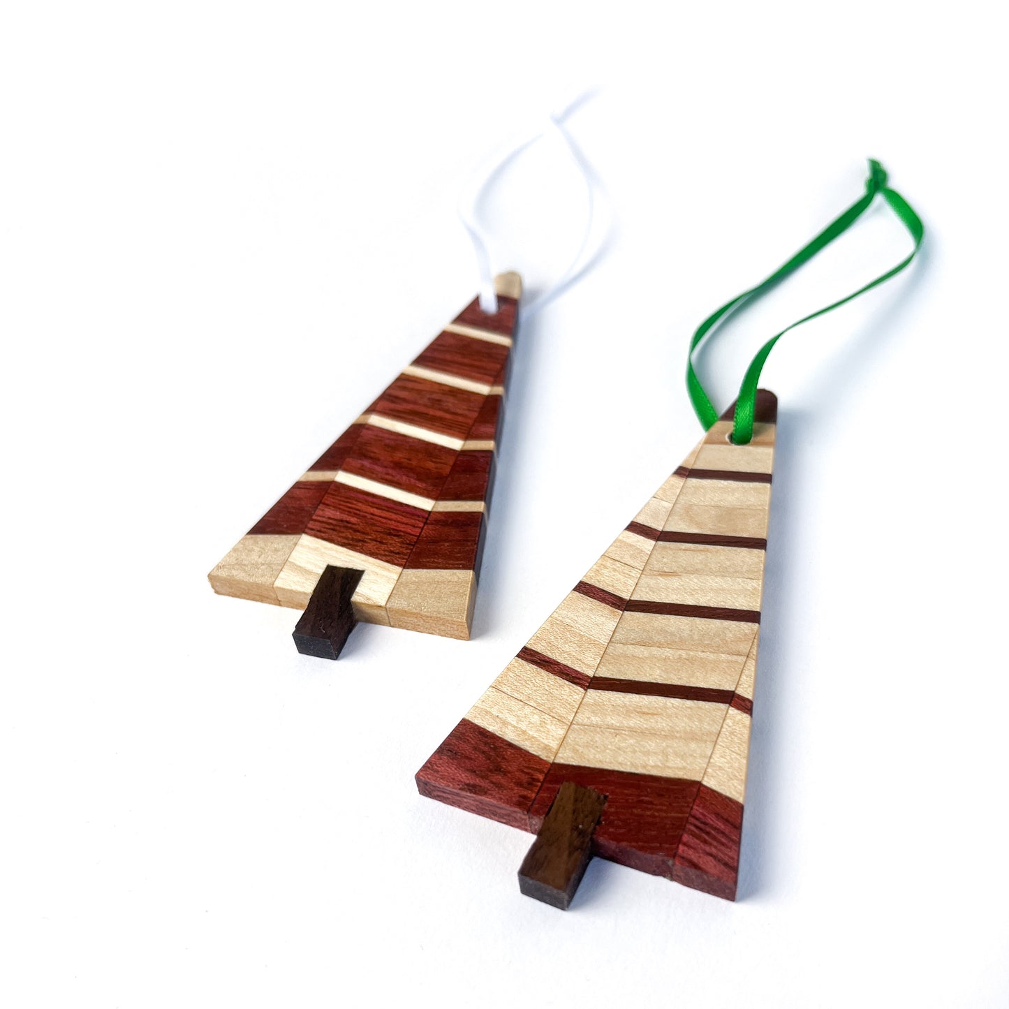 Two wooden Christmas tree ornaments with light and dark striped designs, one with a white ribbon and one with a green ribbon.