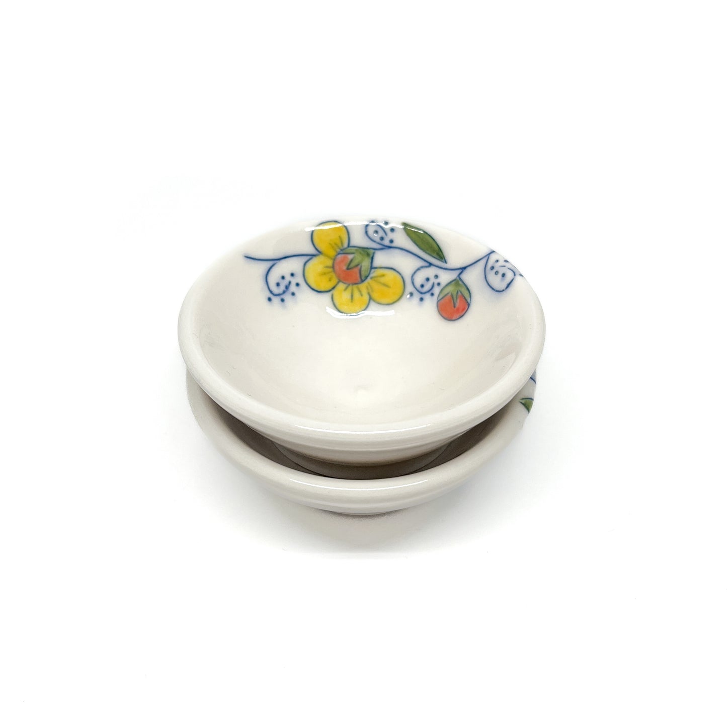 Two small ceramic dishes stacked; the top one has yellow flowers, blue swirls, and green and red leaves.