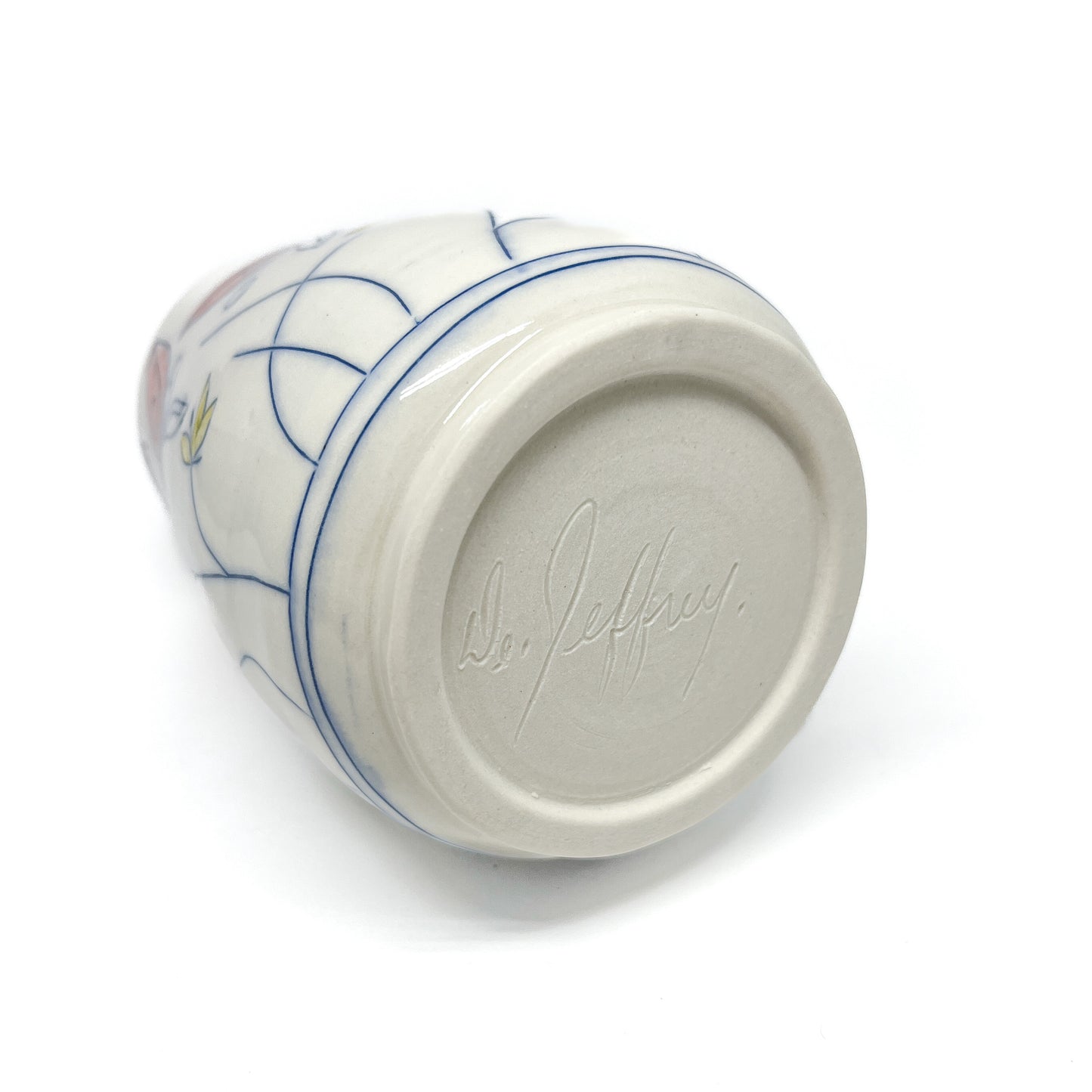 The bottom of a white ceramic vase with blue floral outlines and colored petal details shows a signature "De. Jeffrey."