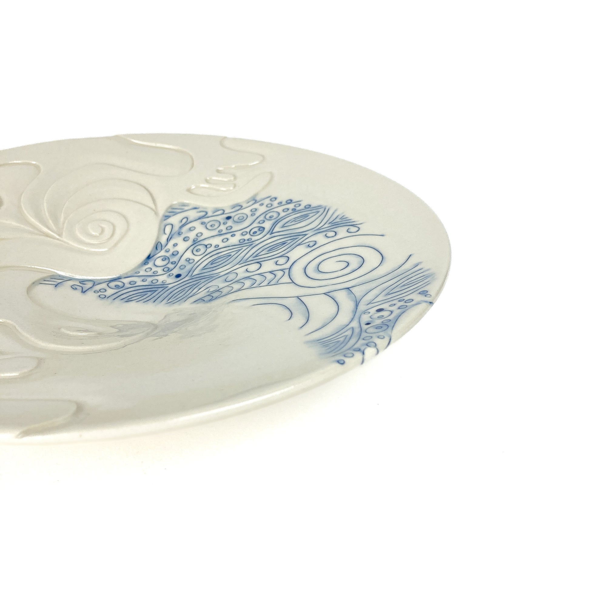 Close-up of a wide handmade pottery plate with carved abstract designs and detailed blue swirling patterns.