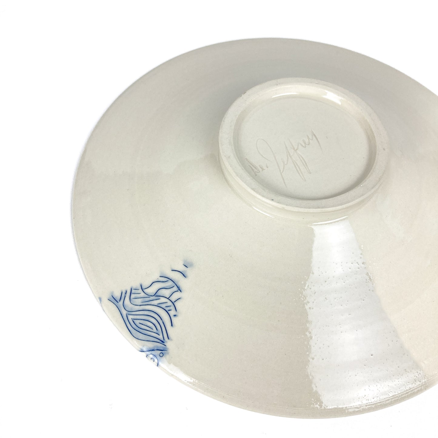 Underside of a wide ceramic plate with a small blue abstract design and a signature.