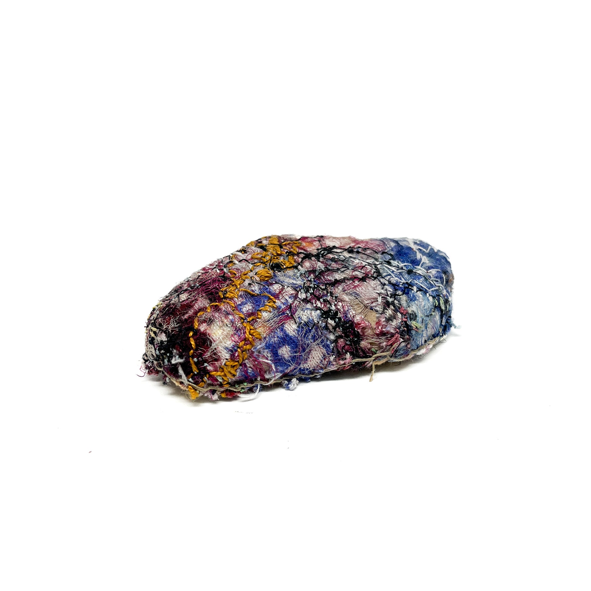 Embroidered Rock: Oval textured textile art resembling a rock, with stitched details in blue, burgundy, yellow, black, and white threads.