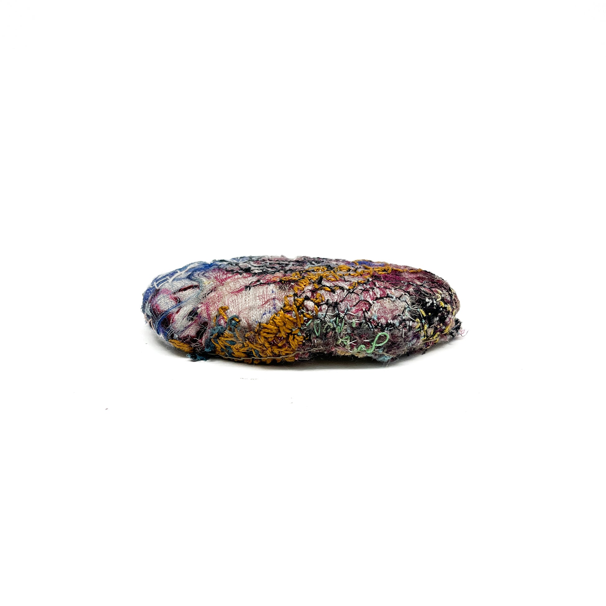 Embroidered Rock: Round textured textile art resembling a rock, with stitched details in various colorful threads.