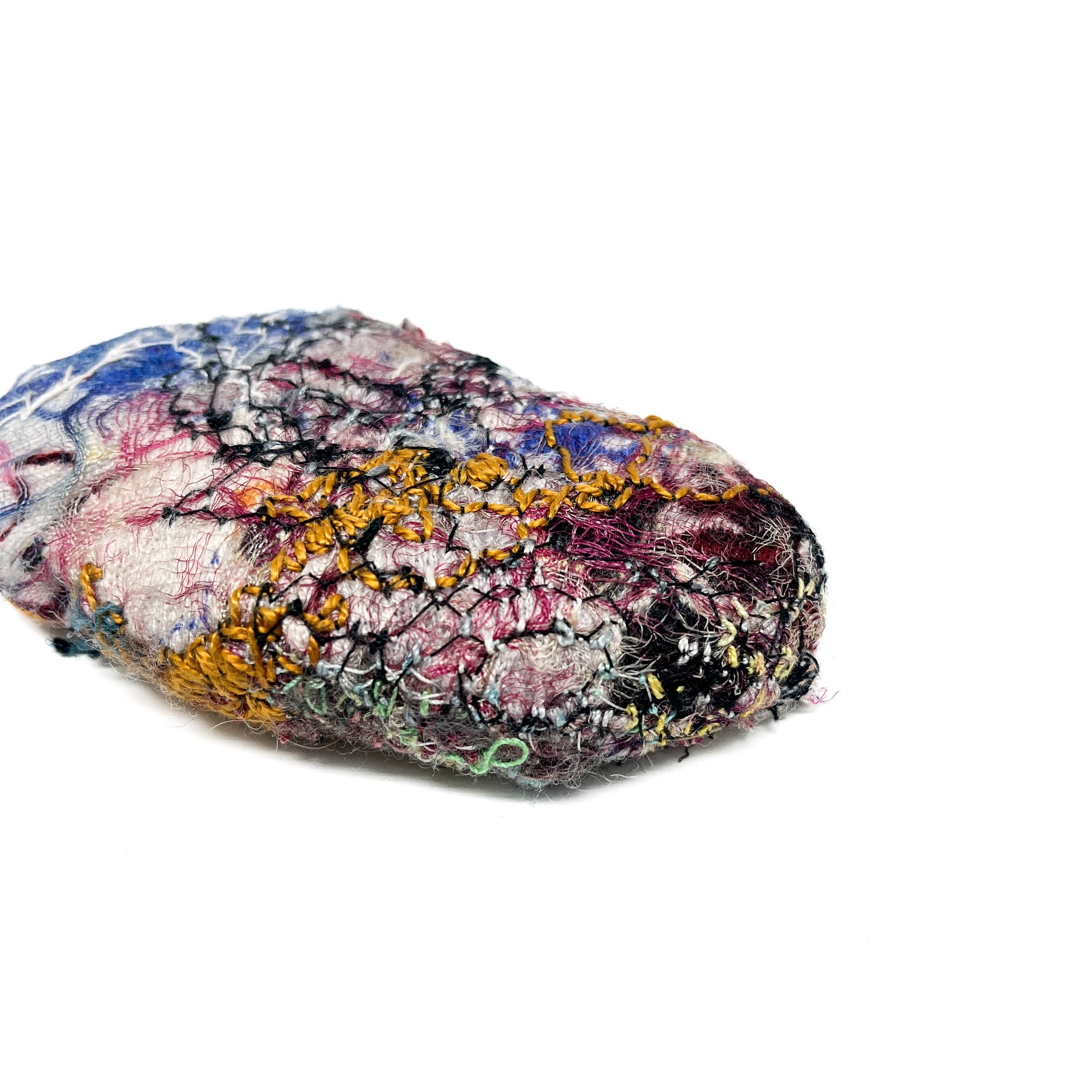 Embroidered Rock by Jane Kenyon: Textured textile art resembling a rock, with intricate stitching in blue, pink, yellow, black, and green threads.