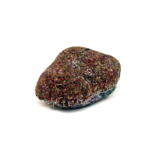A textured rock, covered with layers of dense, colorful stitching and embroidery, creating a tactile surface.