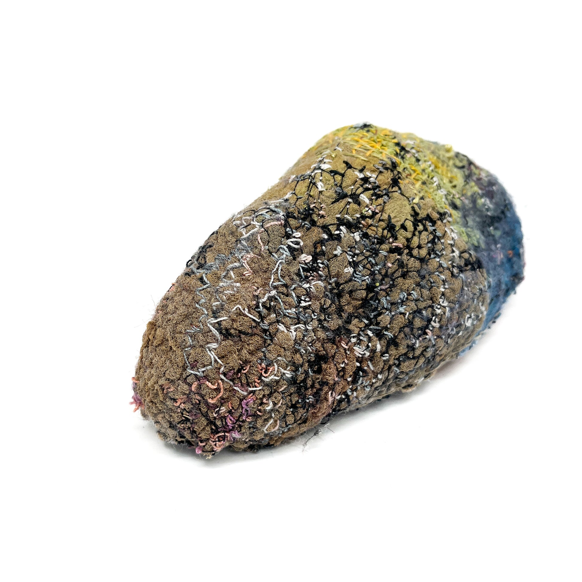 A uniquely textured rock, its surface features layers of colorful and intricate embroidery and stitching.