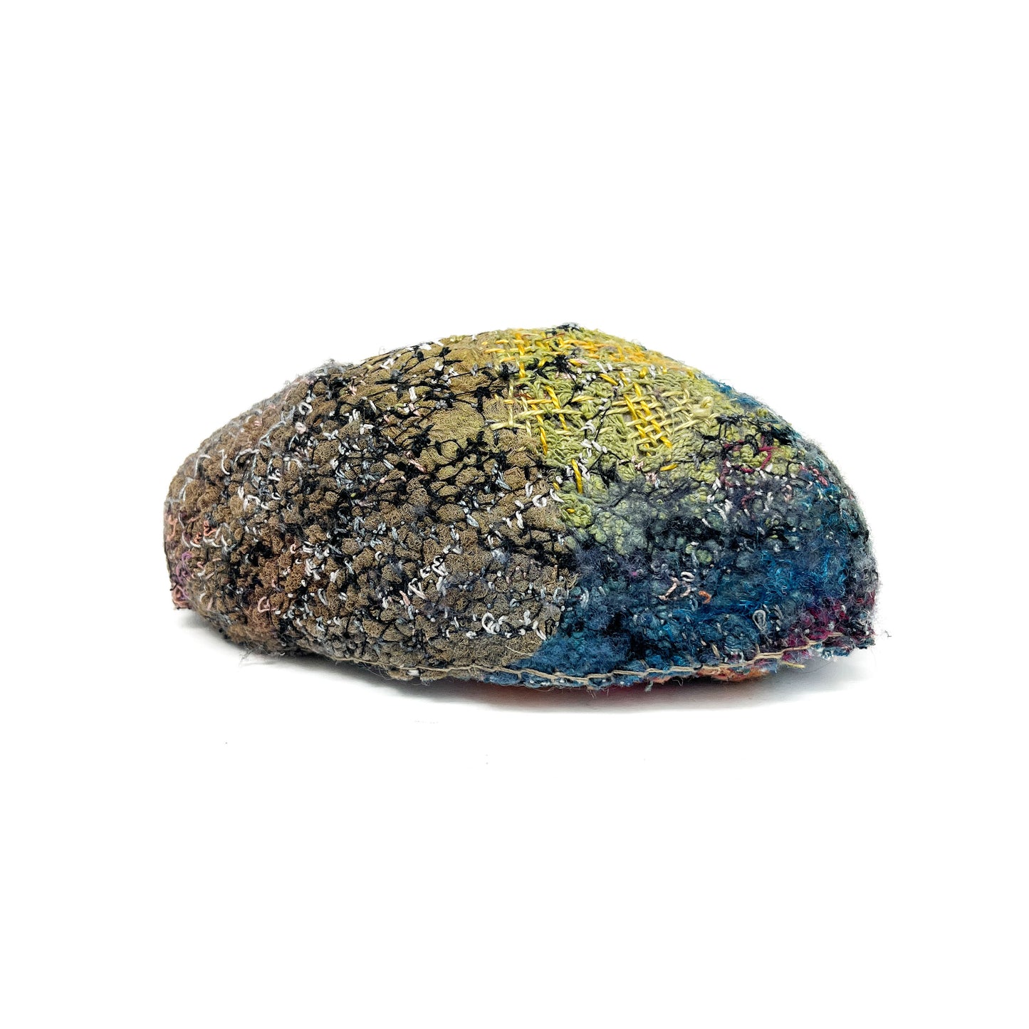 A textured rock displays layers of colorful and elaborate embroidery and stitching across its surface.