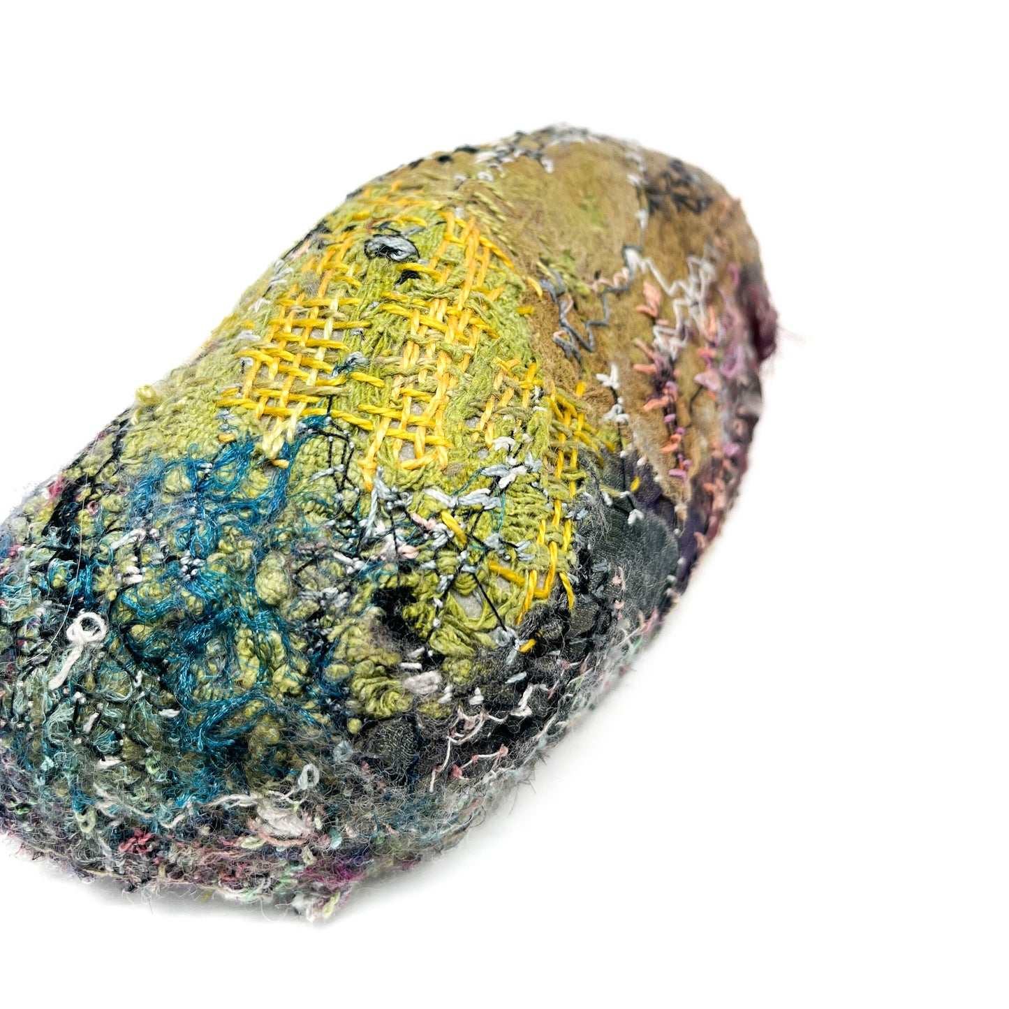 A rock showcases a rich and varied texture from layers of colorful, detailed embroidery and stitching.