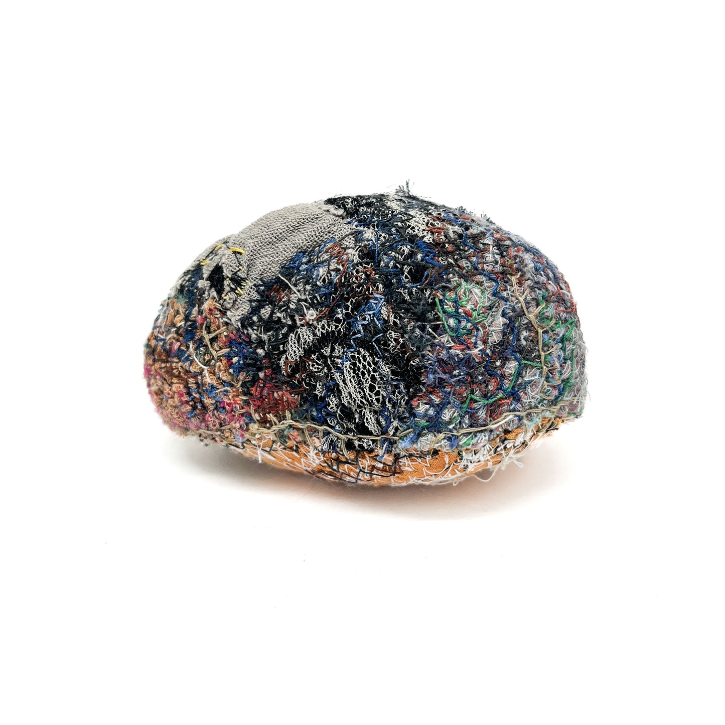 A rounded rock features a dense and colorful surface of intricate embroidery and various stitching textures.
