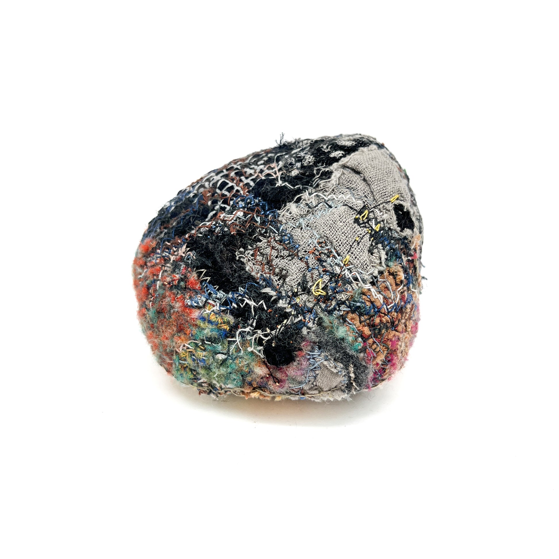 A rock covered in a complex and colorful arrangement of embroidery and stitching, creating a unique tactile quality.