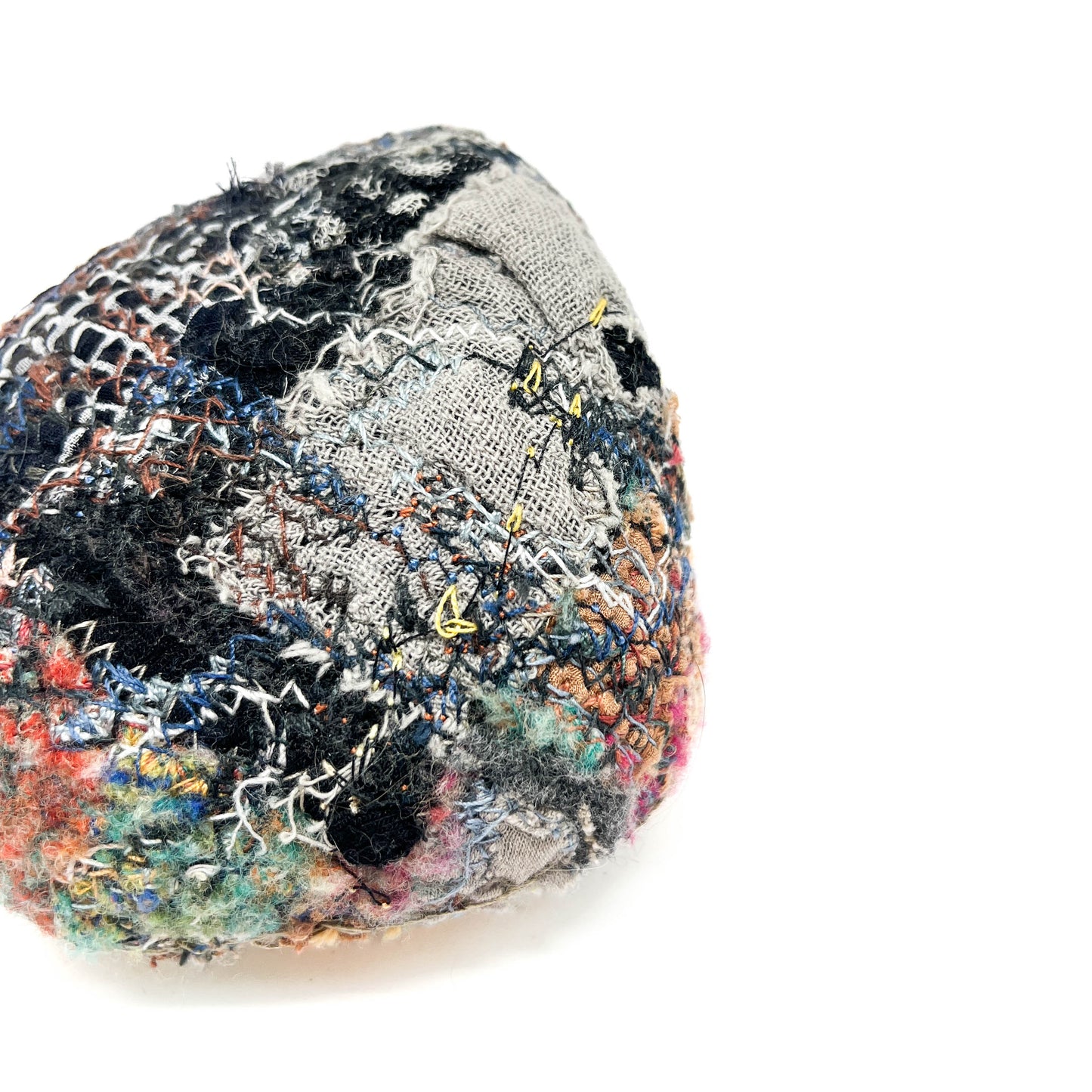 A uniquely textured rock by Jane Kenyon, features layers of colorful, intricate embroidery and stitching.
