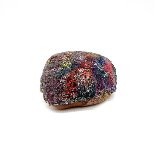 A stone with a richly textured surface created by layers of colorful and dense embroidery and stitching.