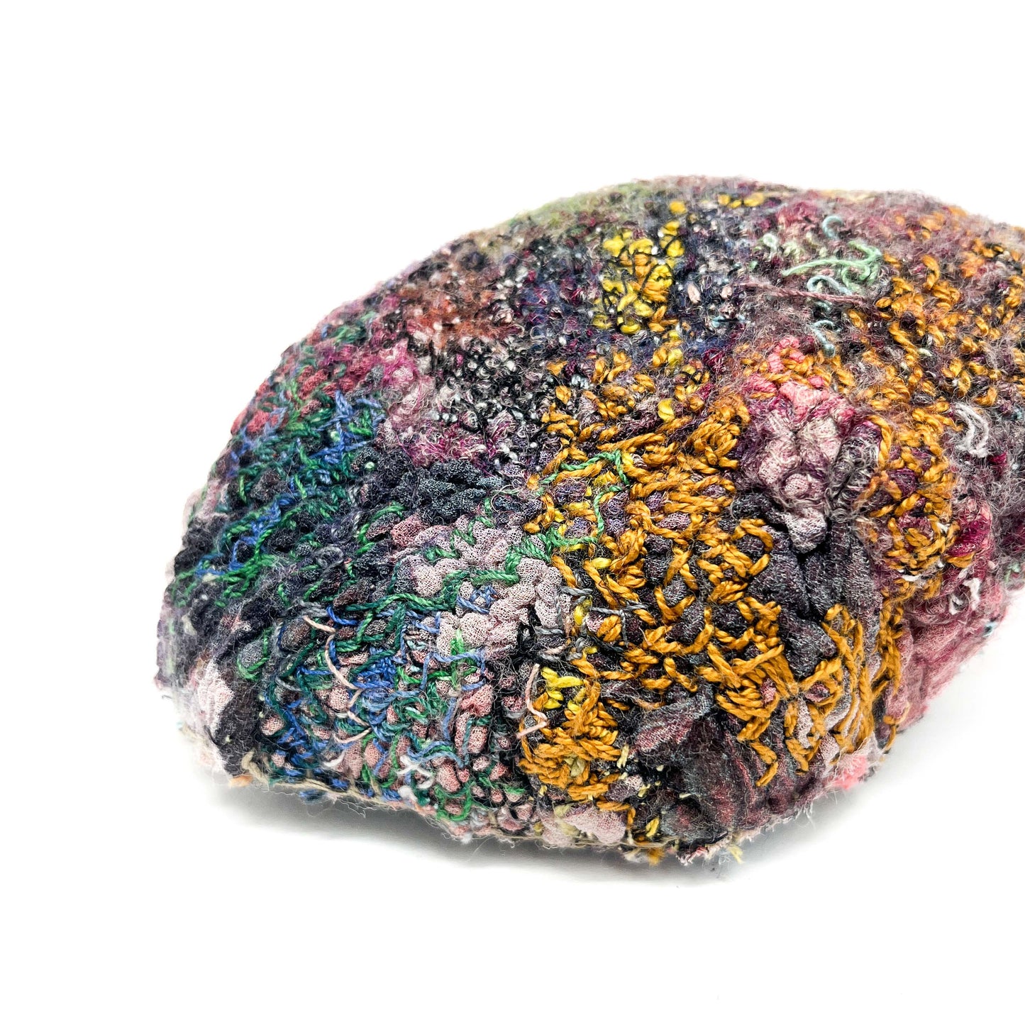 A stone with a complex, textured surface created by layers of colorful and detailed embroidery and stitching.