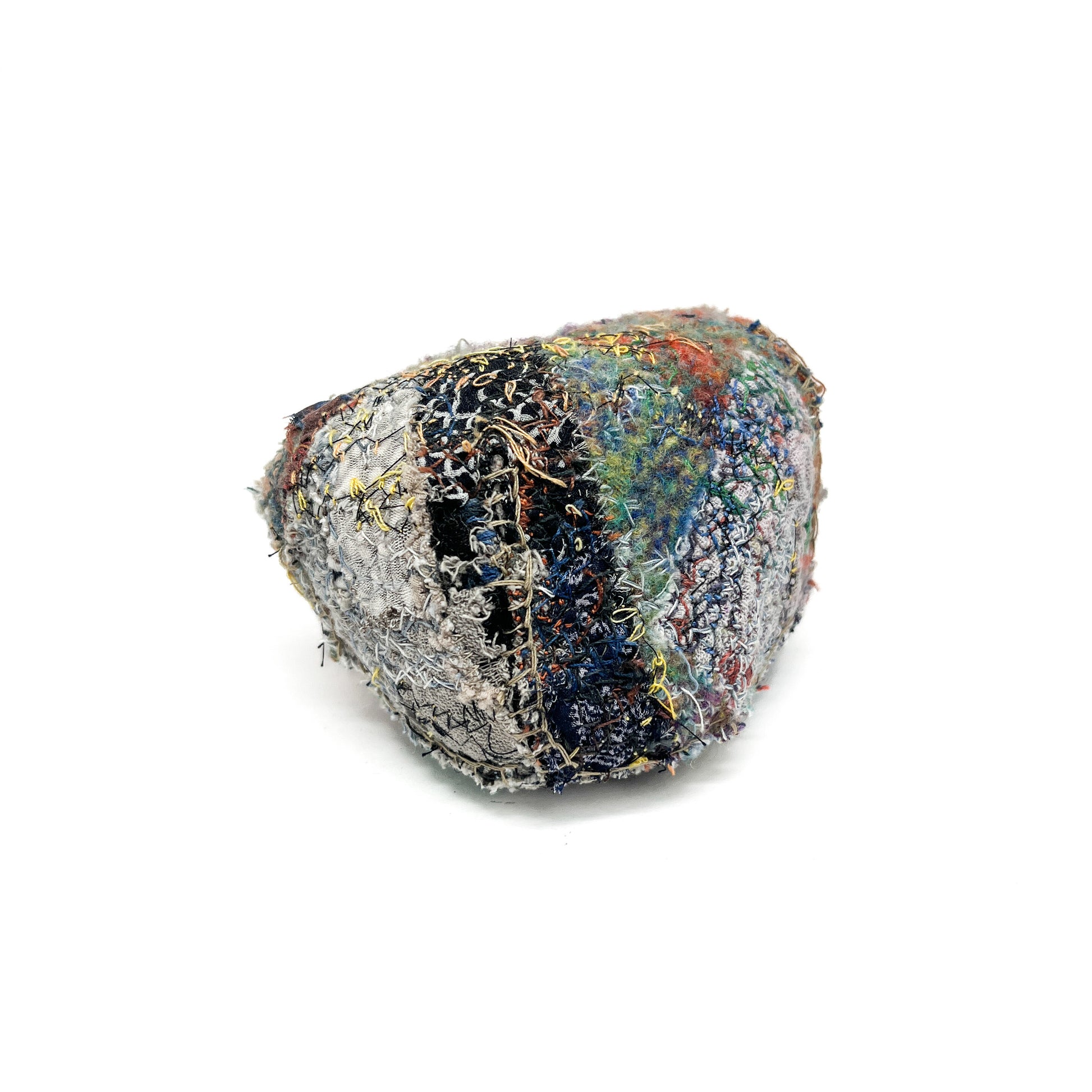 A stone by Jane Kenyon, features a textured surface of colorful and elaborate embroidery and stitching.
