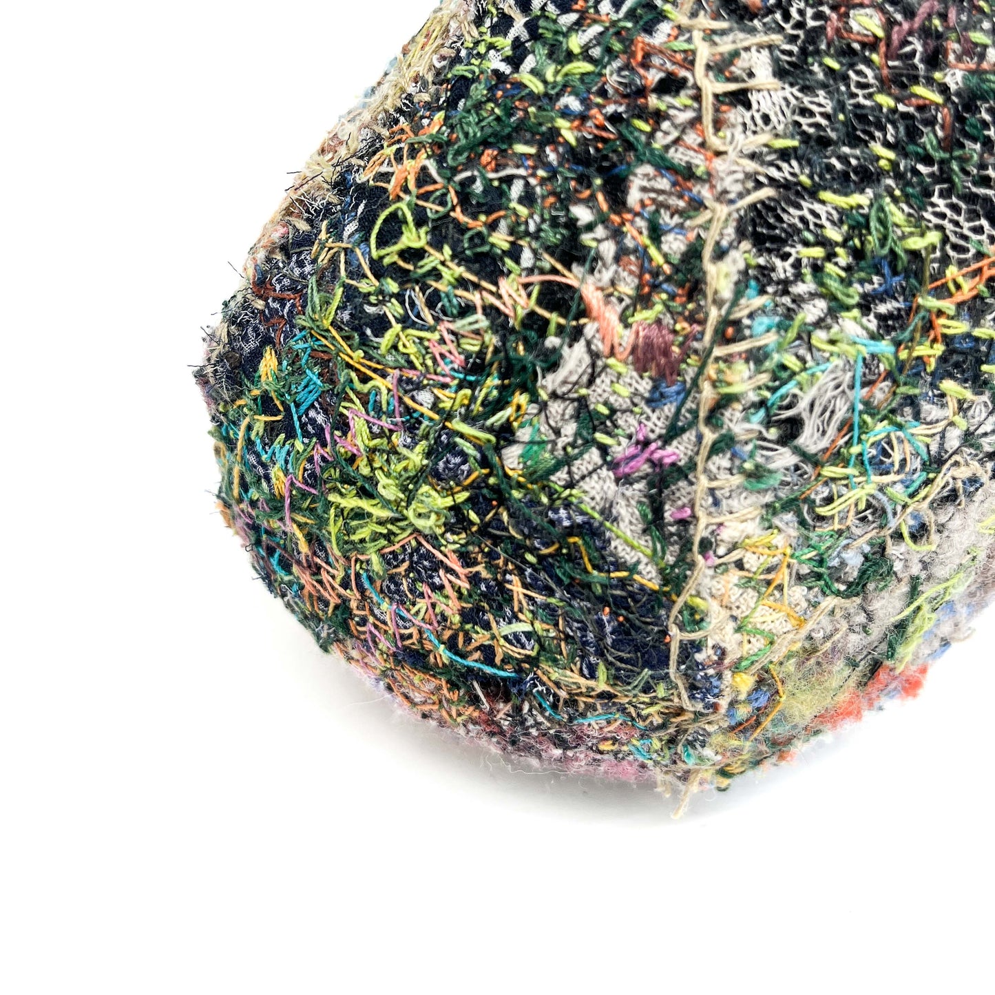 A stone showcases a textured surface of colorful, dense embroidery and stitching.