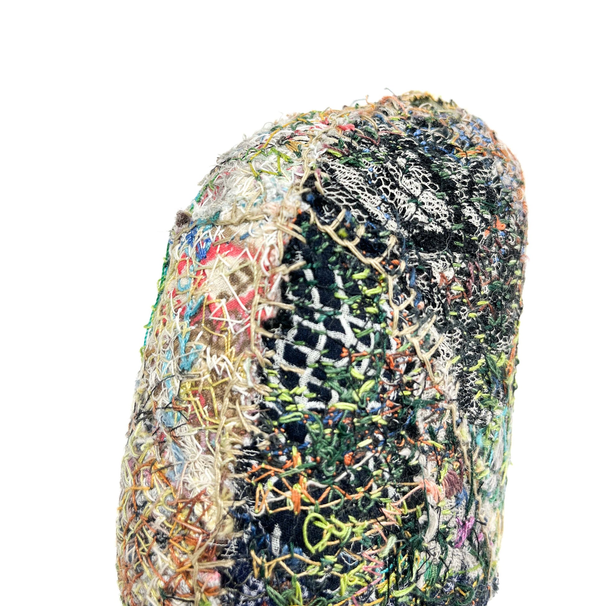 A close-up of a textured stone covered in layers of colorful and intricate embroidery and stitching.