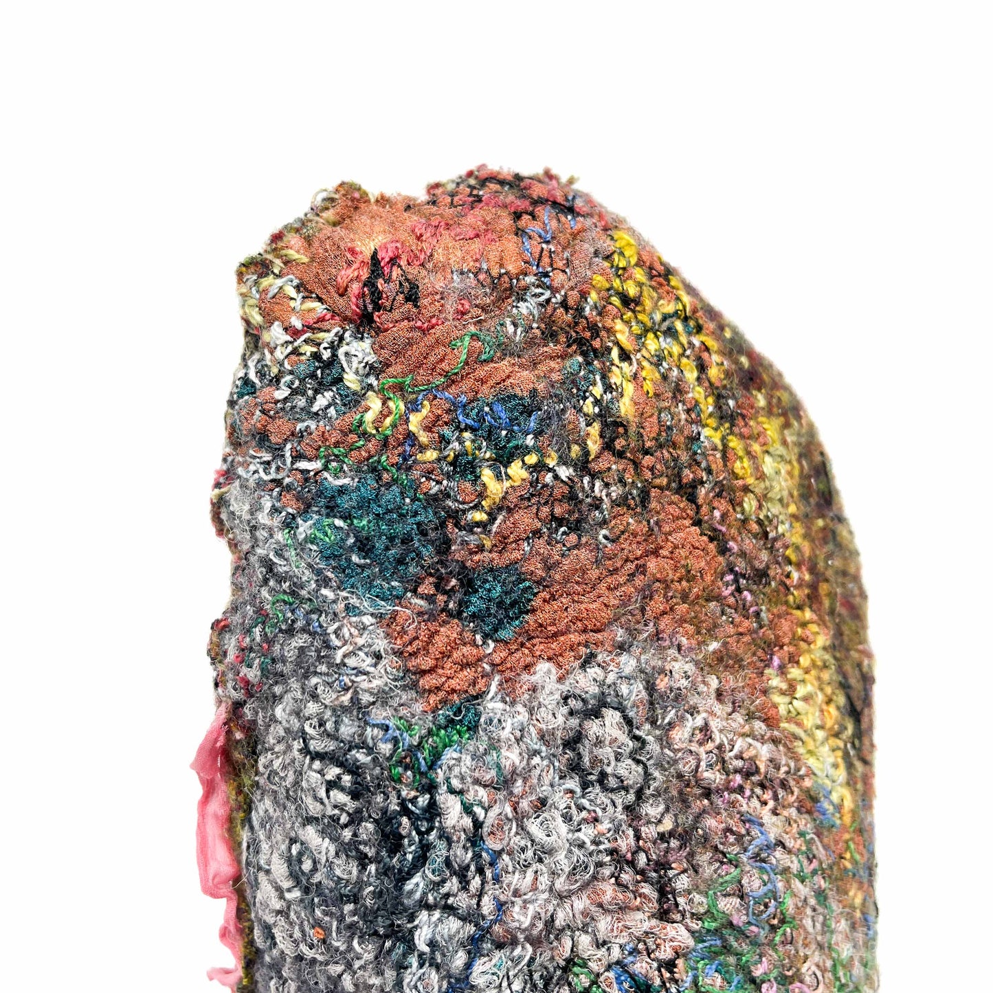 A textured stone covered in colorful and intricate embroidery and stitching, accented by a delicate pink fabric.