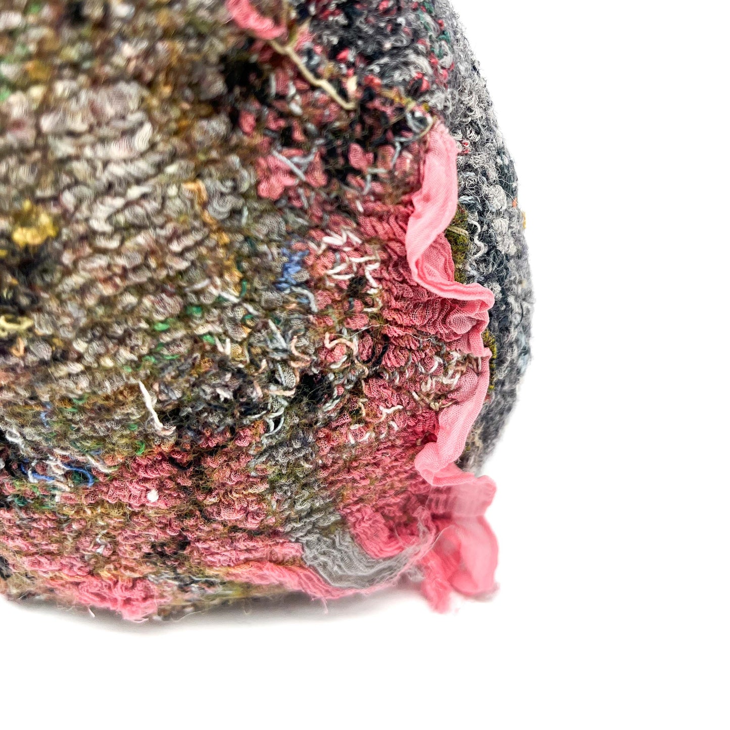 A close-up shows a textured stone with layers of colorful embroidery and stitching, and a soft pink fabric detail.