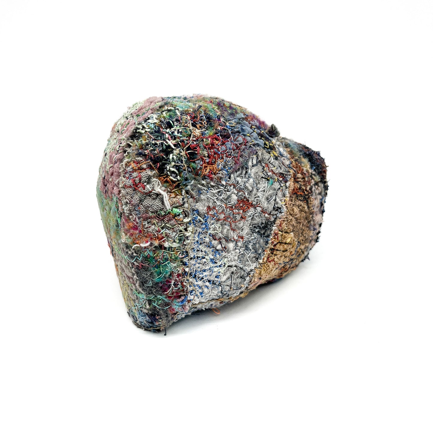 A textured stone features a complex surface of colorful, interwoven embroidery and stitching.