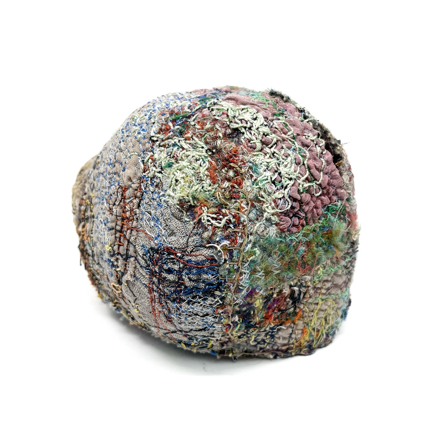 A textured stone displays layers of colorful and intricate embroidery and stitching across its surface.