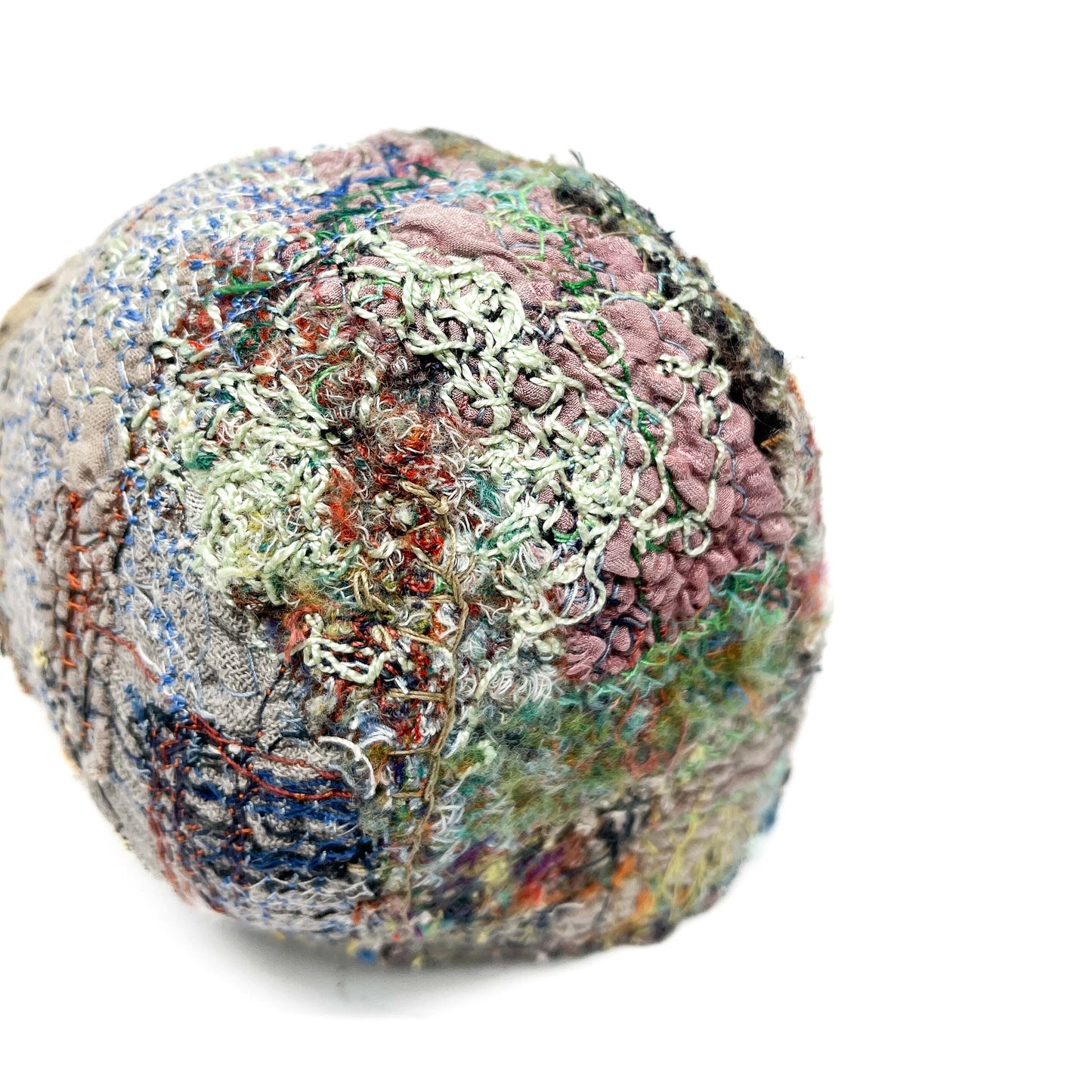 A textured stone features a complex surface of colorful and intricate embroidery and stitching details.